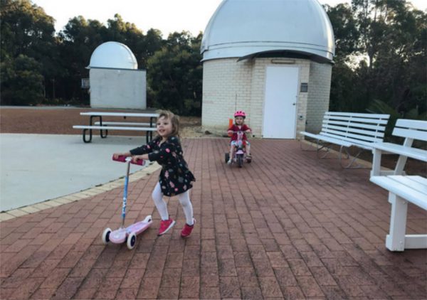 Rhemi and Ella riding a bike and scooter up at the Observatory's viewing area. Image Credit: Roger Groom
